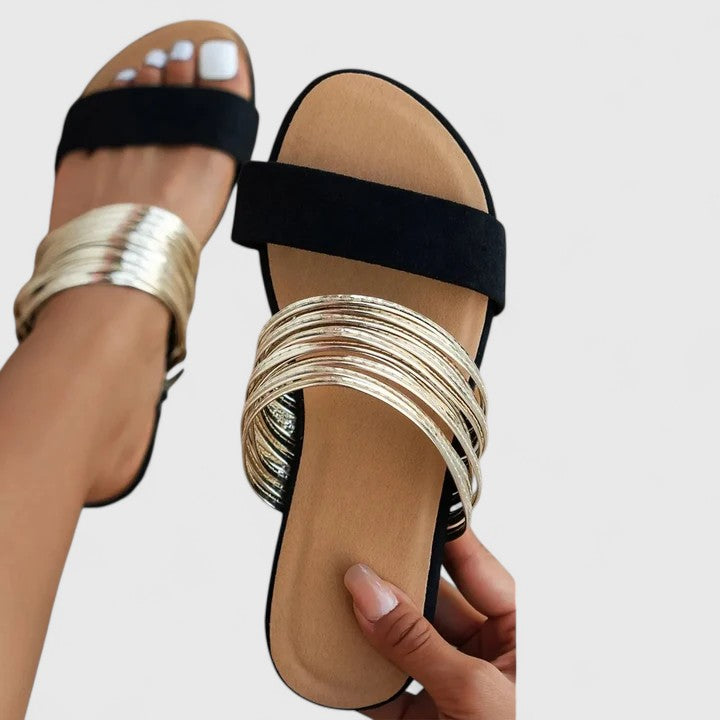 A woman wearing metallic golden slip-on slide sandals with a double strap on a summer evening.