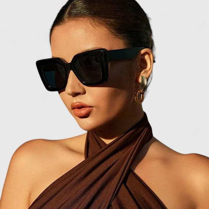 A woman at golden hour wearing bold geometric sunglasses, poised and glamorous in the sun.