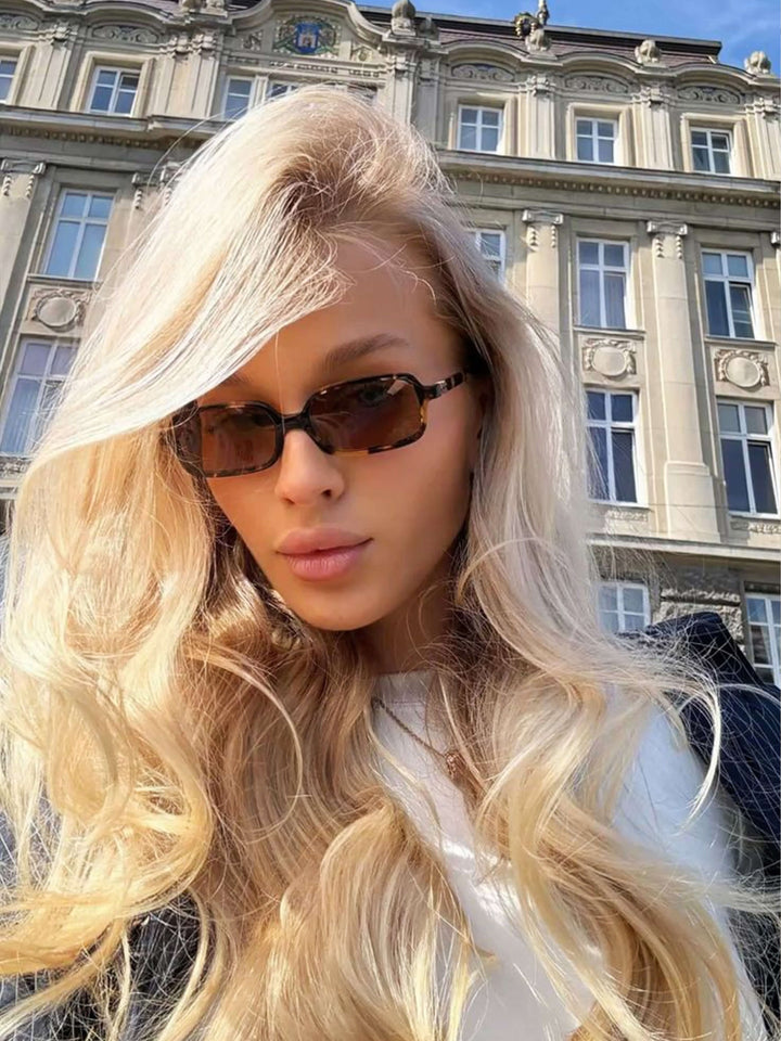 A woman walking through town wearing small rectangular sunglasses with a relaxed, polished look.