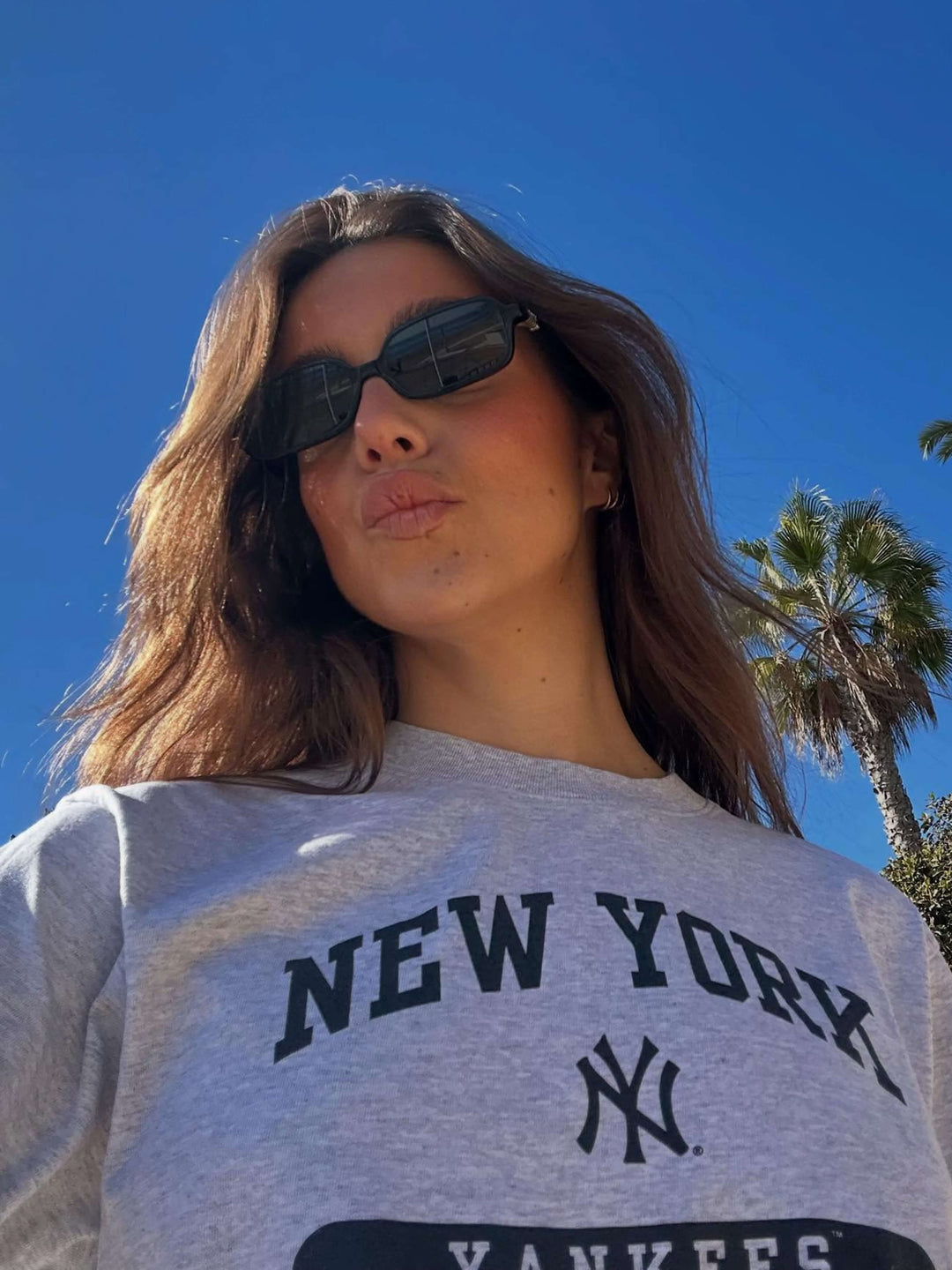 A woman walking through town wearing small rectangular sunglasses with a relaxed, polished look.