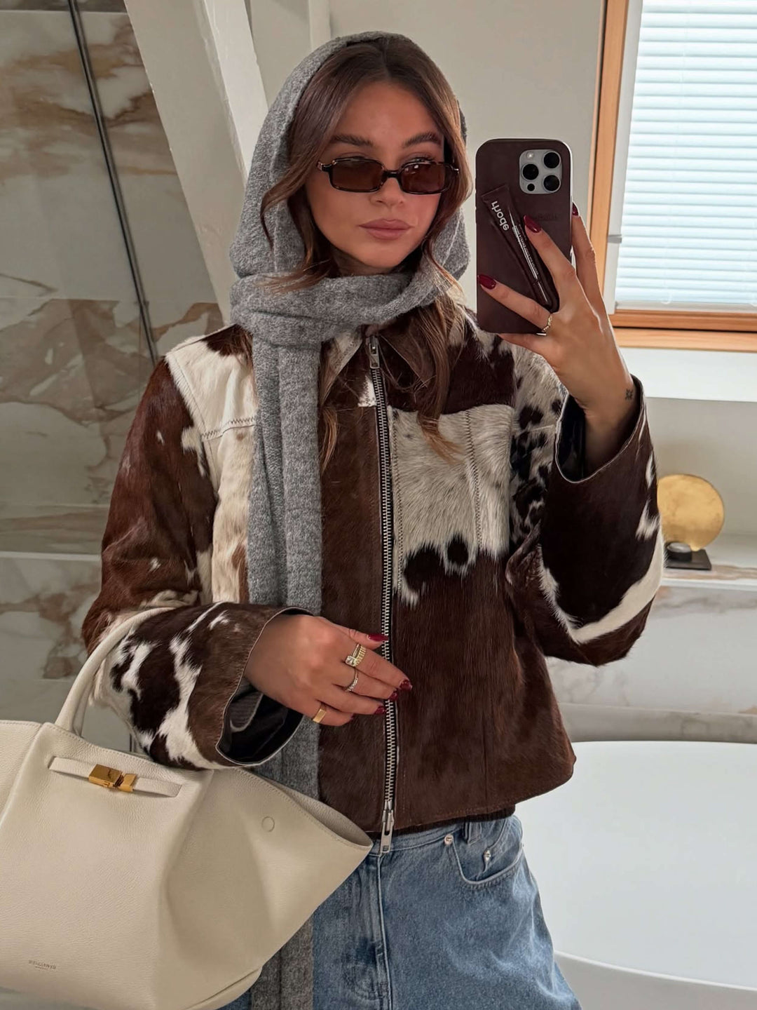 A woman walking through town wearing small rectangular sunglasses with a relaxed, polished look.