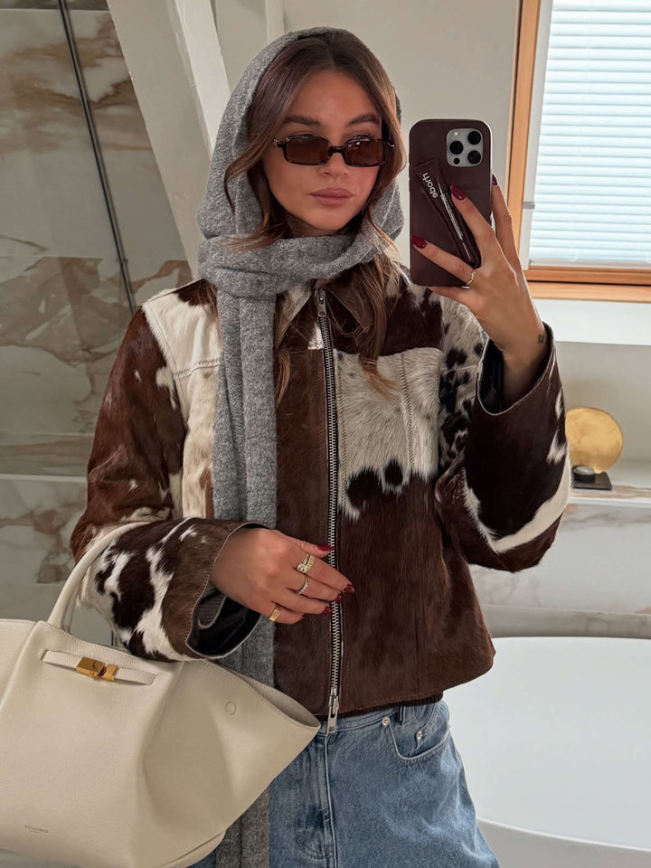 A woman walking through town wearing small rectangular sunglasses with a relaxed, polished look.