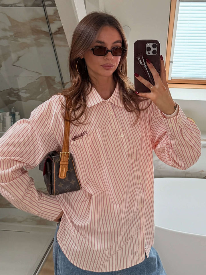 A woman walking through town wearing small rectangular sunglasses with a relaxed, polished look.
