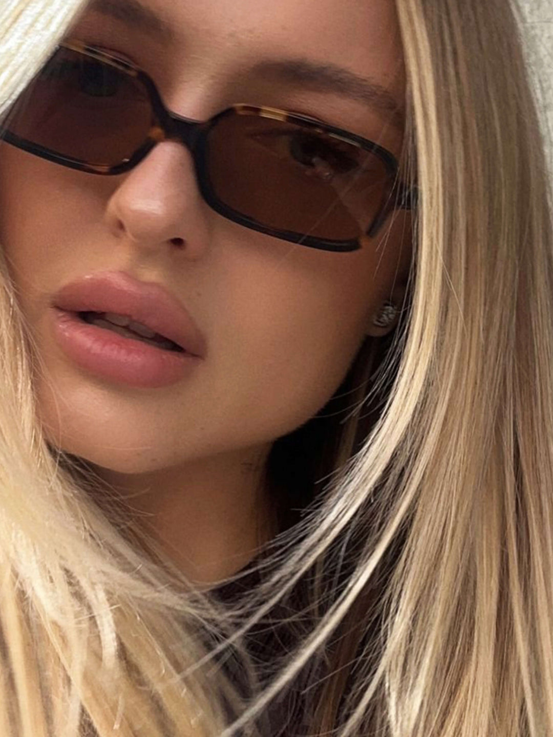 A woman walking through town wearing small rectangular sunglasses with a relaxed, polished look.