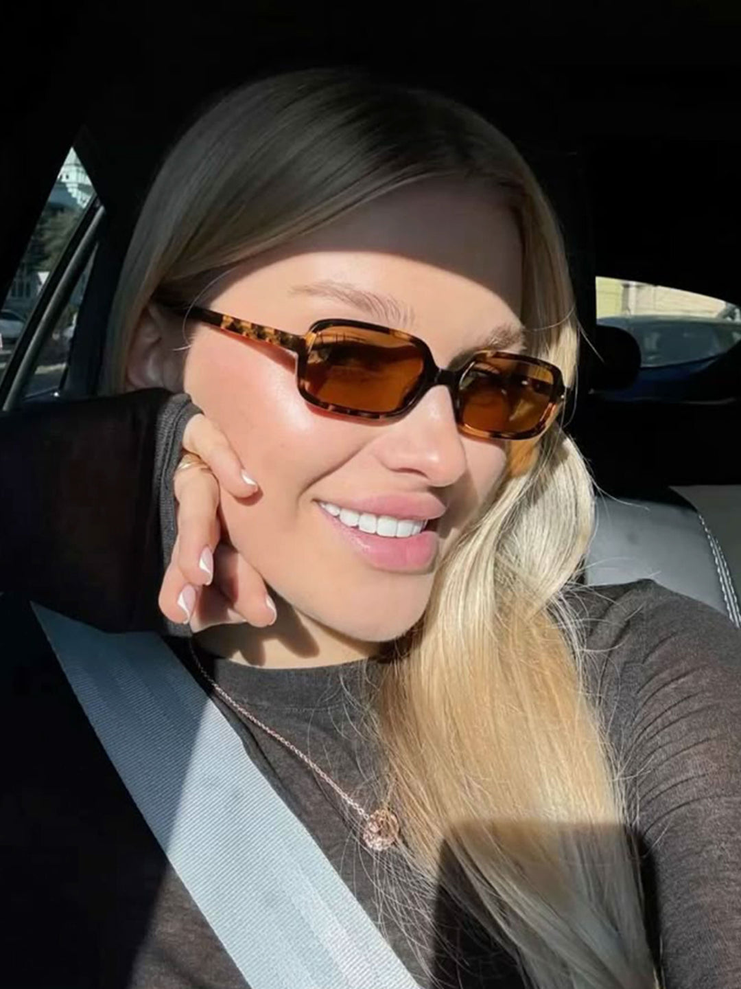 A woman walking through town wearing small rectangular sunglasses with a relaxed, polished look.