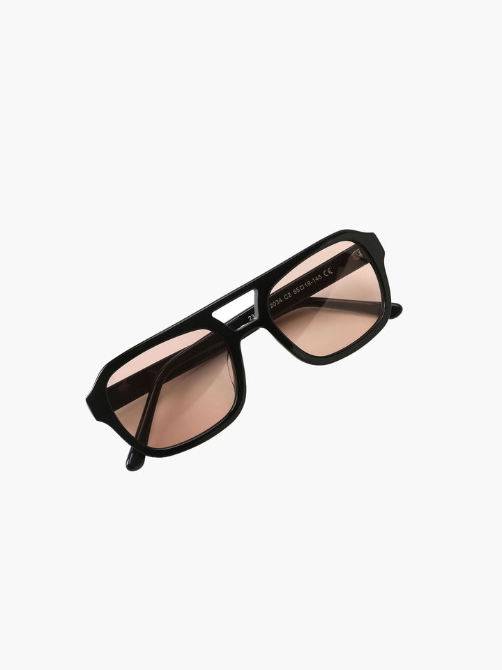 A woman wearing oversized tortoiseshell aviator sunglasses with green-tinted lenses on a sunny day outdoors.