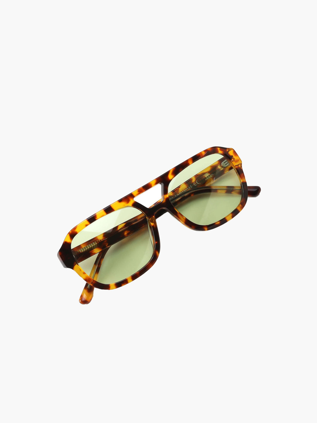 A woman wearing oversized tortoiseshell aviator sunglasses with green-tinted lenses on a sunny day outdoors.