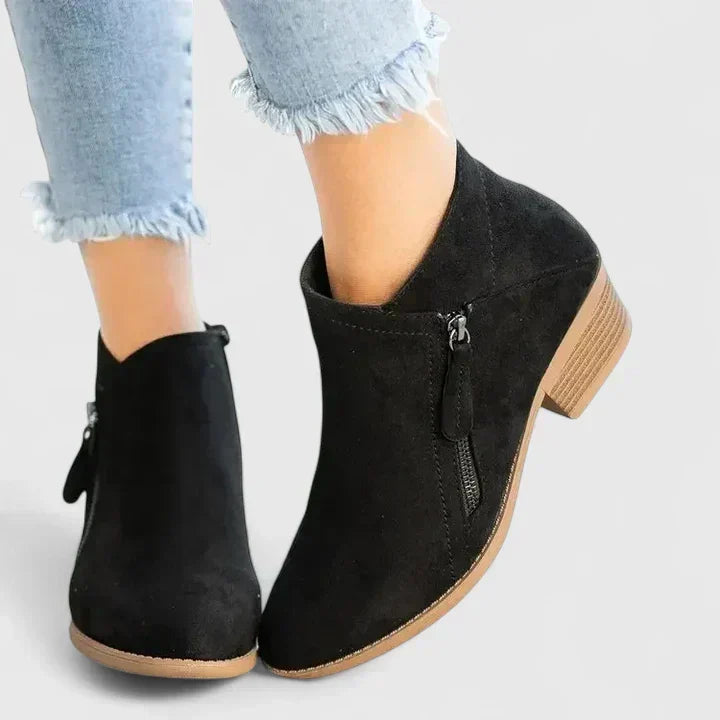 Woman wearing black side-zip ankle boots, stepping off a kerb in town.