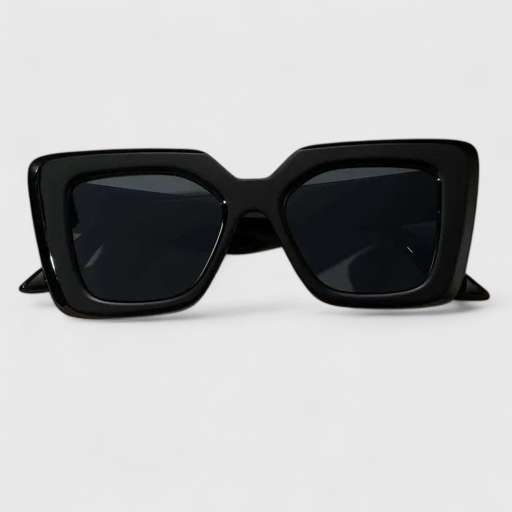 A woman at golden hour wearing bold geometric sunglasses, poised and glamorous in the sun.