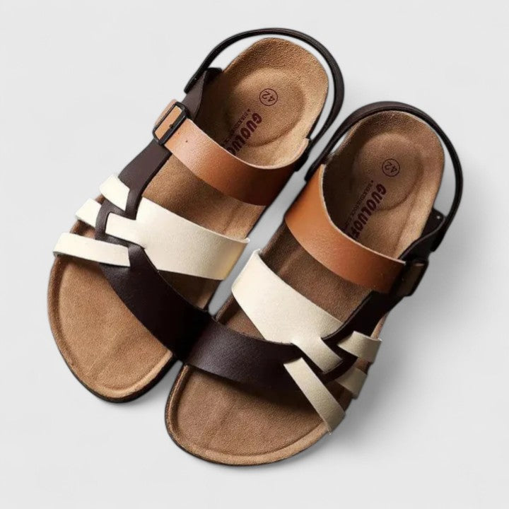 A woman wearing cream and brown multi-strap supportive sandals, standing steady and relaxed on a sunny path.
