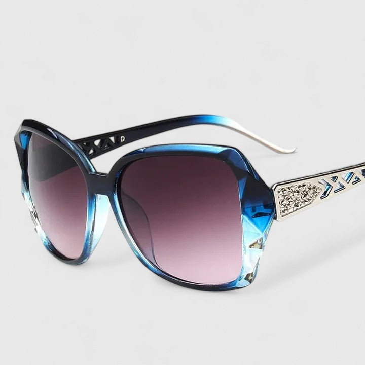 A woman on a sunny city street wearing chic square-frame sunglasses, smiling confidently.
