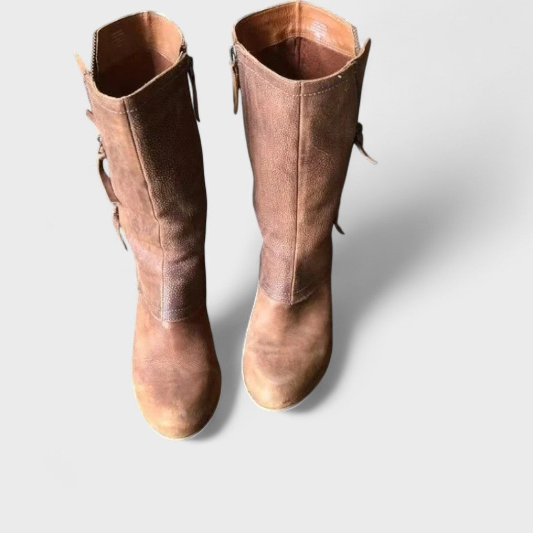A woman in slim jeans wearing brown mid-calf boots with buckle detailing and a squared heel.