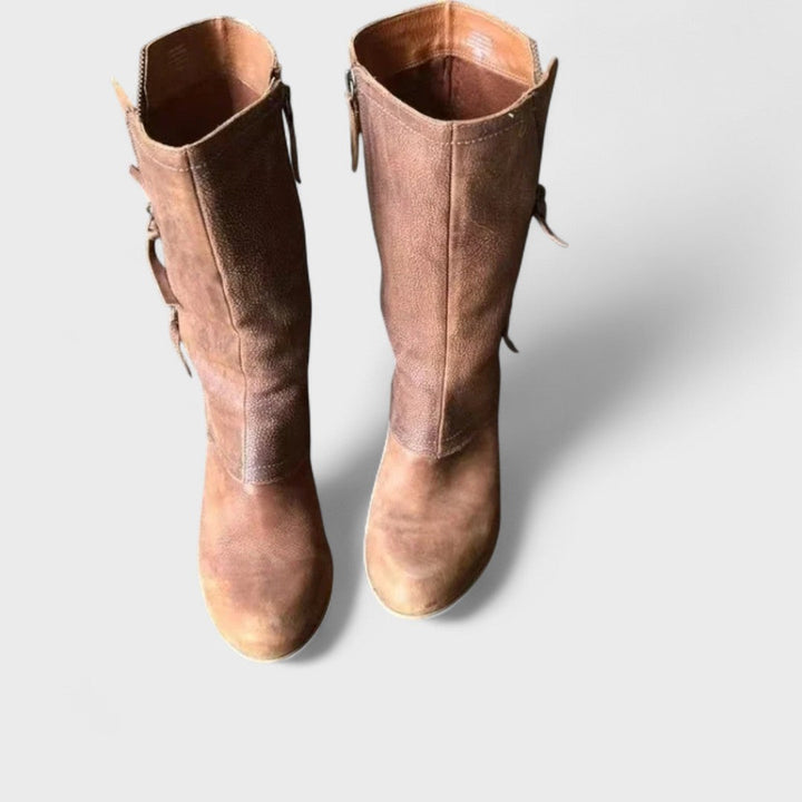 A woman in slim jeans wearing brown mid-calf boots with buckle detailing and a squared heel.