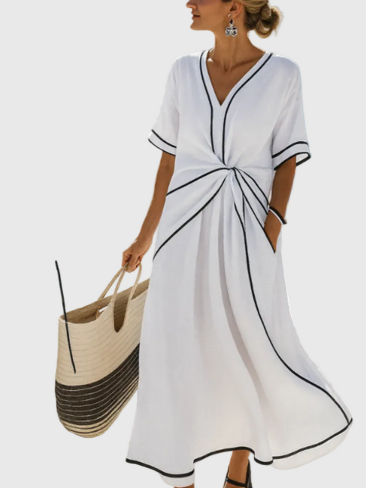 Woman wearing a long flowing maxi dress with an elegant draped detail, standing in warm sunlight.