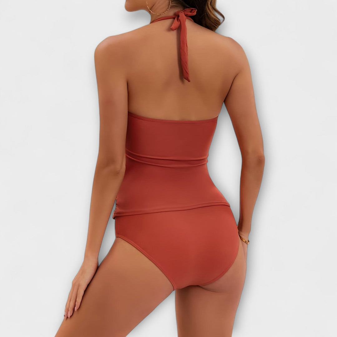 A woman by the water in a solid-colour two-piece halter swimsuit, relaxed and confident in the sun.