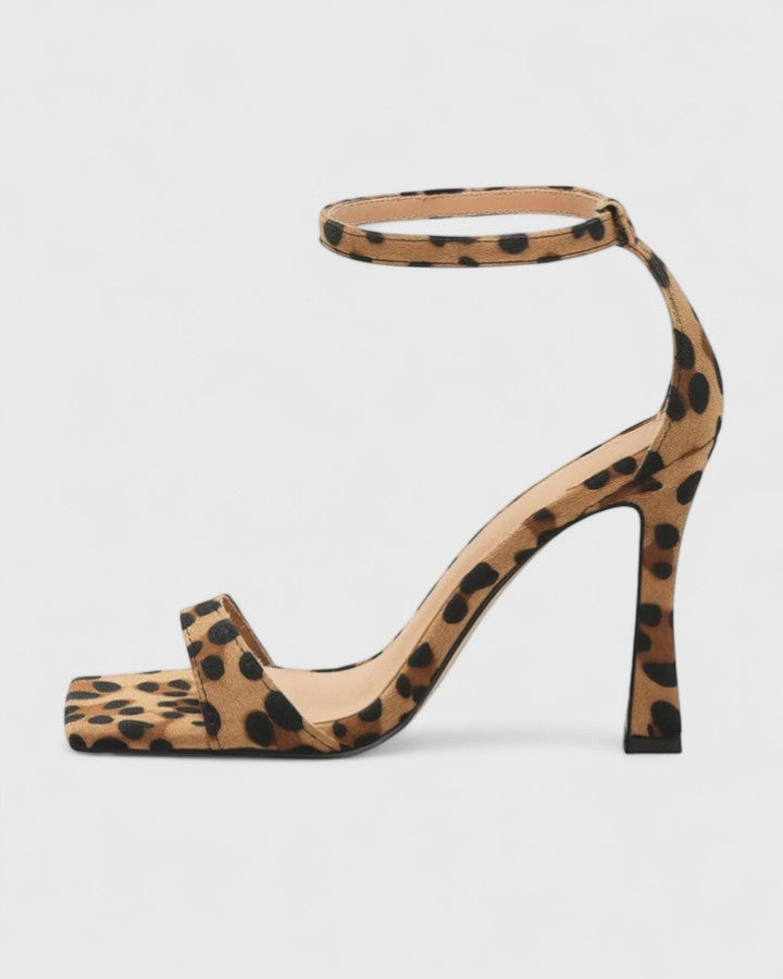 A woman wearing leopard print strappy heels with a square open toe and a thin ankle strap on a night out.