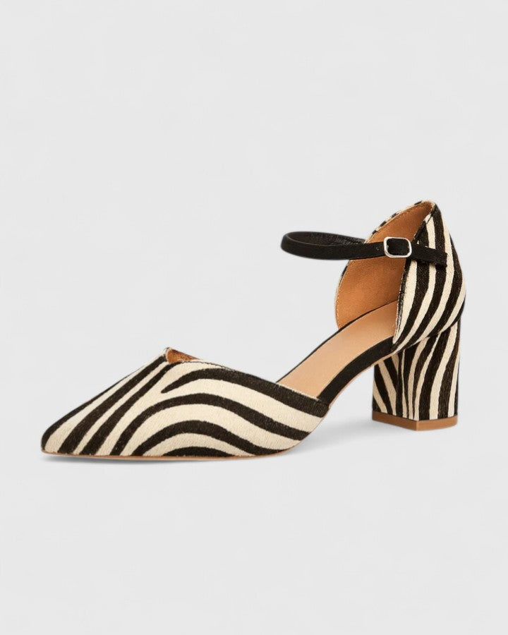 A woman wearing zebra-print block heels with a pointed toe, open sides and a slim ankle strap.