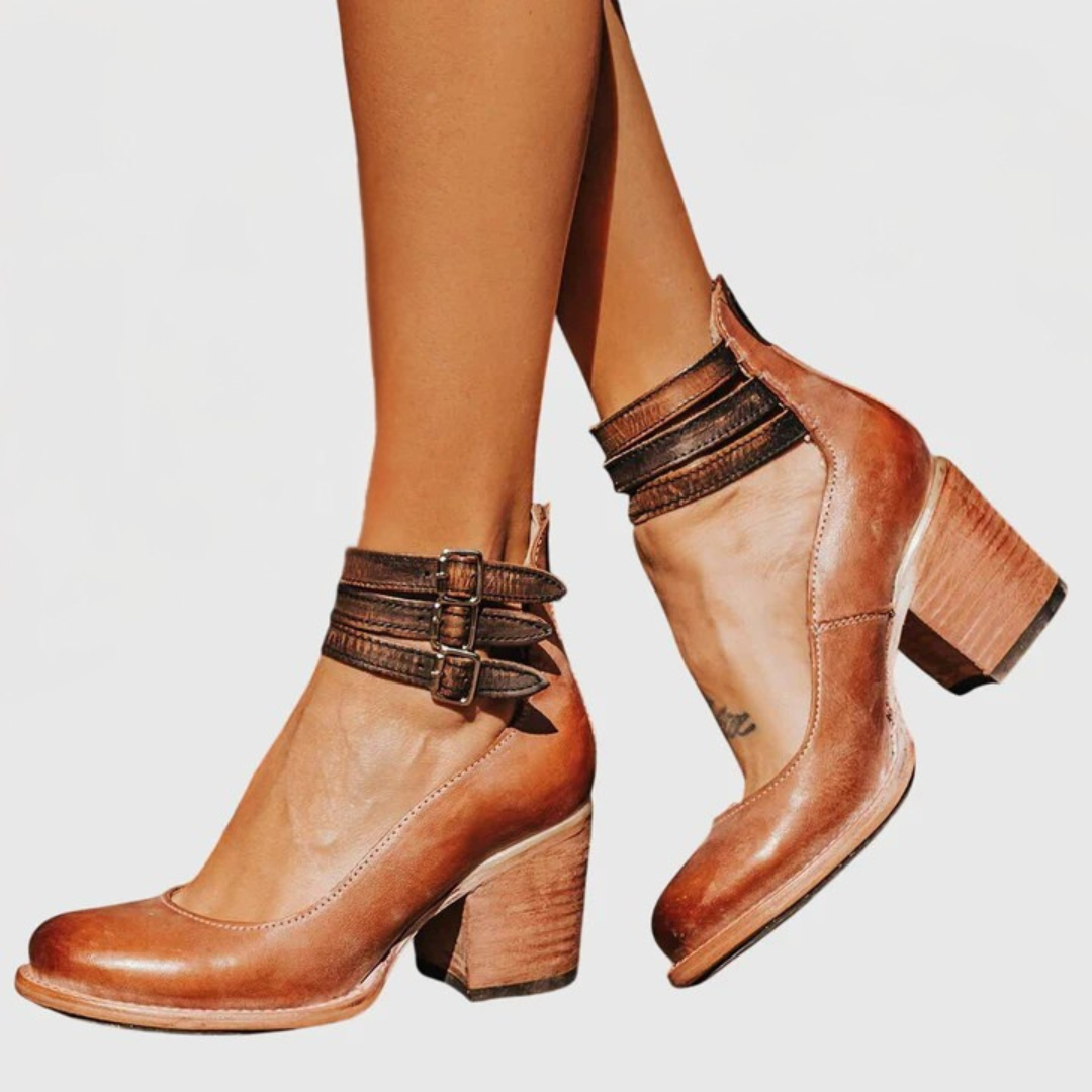 A woman wearing tan block-heel court shoes with buckled ankle straps, walking gracefully in a refined outfit.