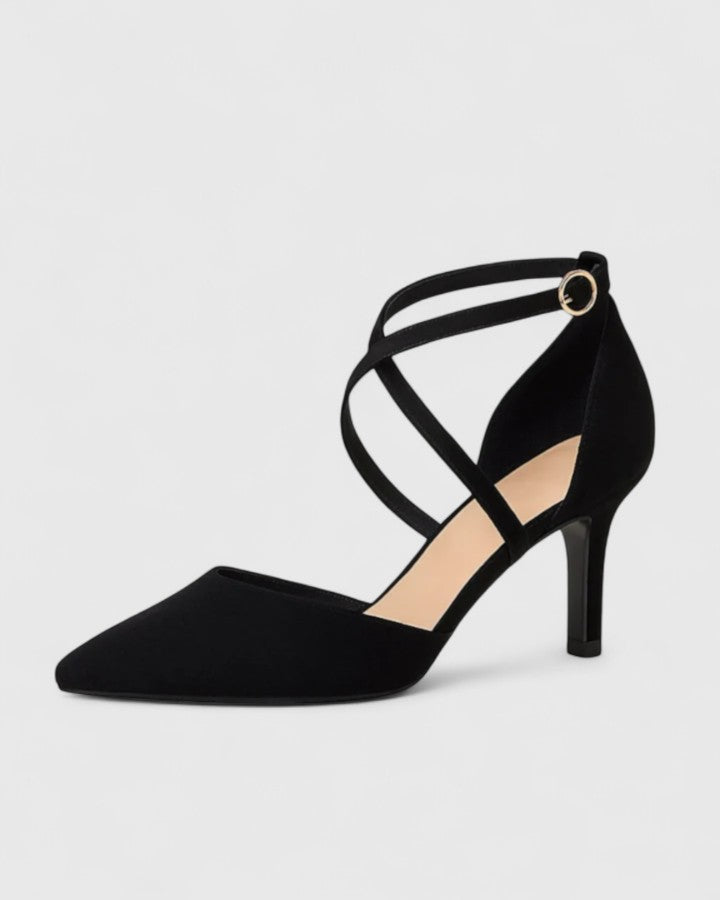 A woman wearing black pointed-toe heels with crossover ankle straps and a slim stiletto heel, dressed for an evening out.