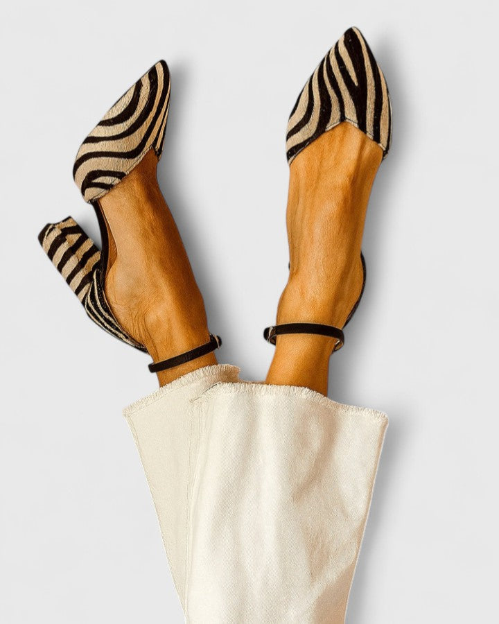 A woman wearing zebra-print block heels with a pointed toe, open sides and a slim ankle strap.