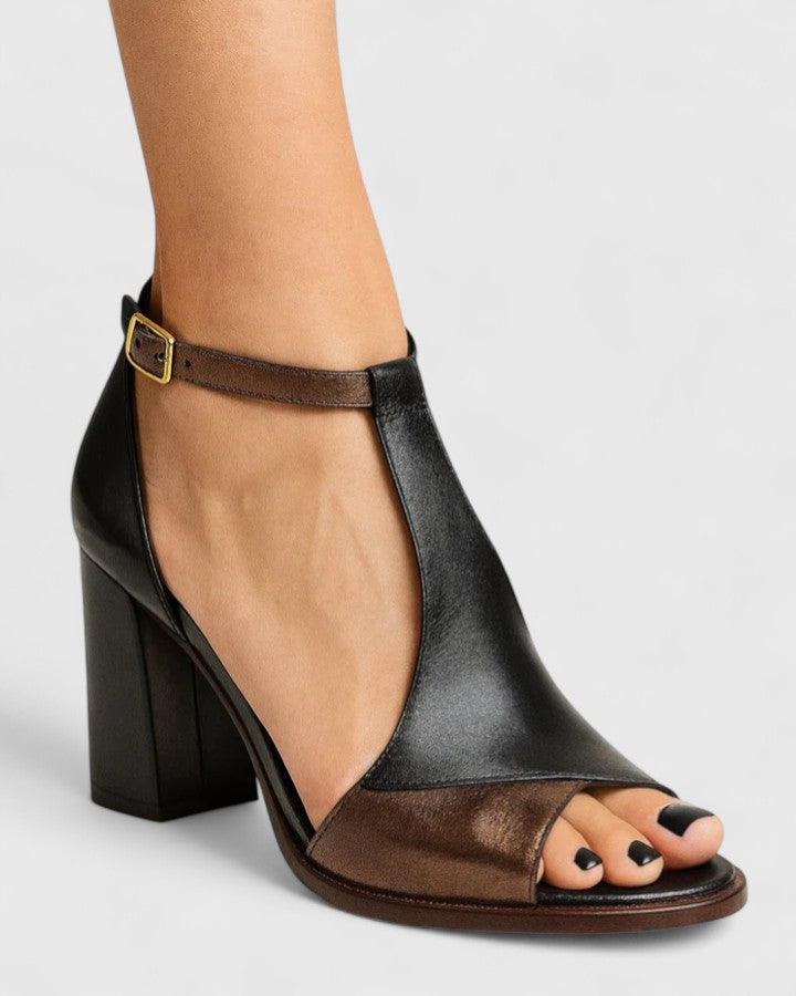 A woman in a black open-toe block heel with an ankle strap, standing confidently at an evening event.