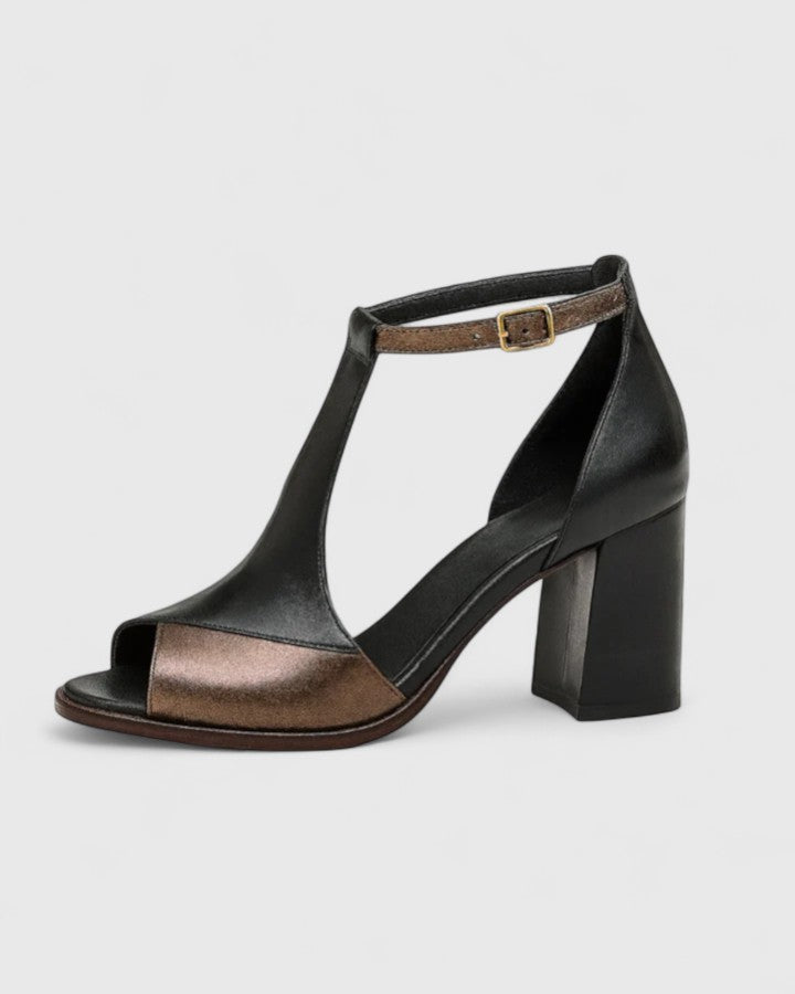 A woman in a black open-toe block heel with an ankle strap, standing confidently at an evening event.