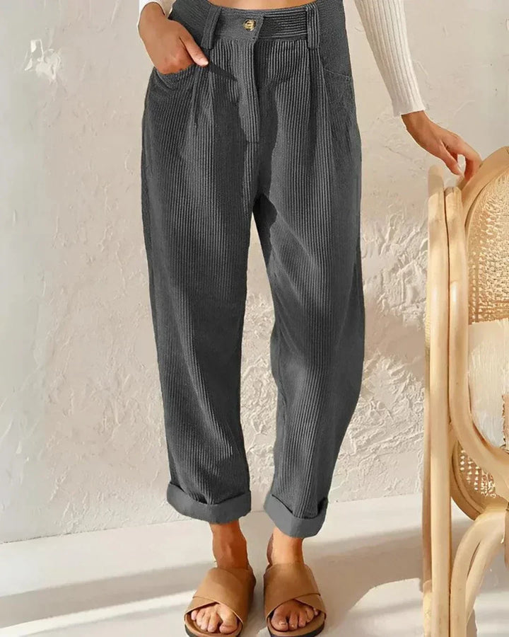 Woman wearing loose high-waisted pants with a tucked-in top, standing in soft light.
