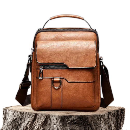 A tan crossbody bag with a flap front, zip pocket and wide adjustable strap on a wooden stump.