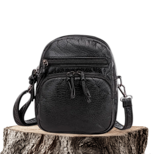 A small black everyday crossbody bag with zip pockets and an adjustable strap on a wooden stump.