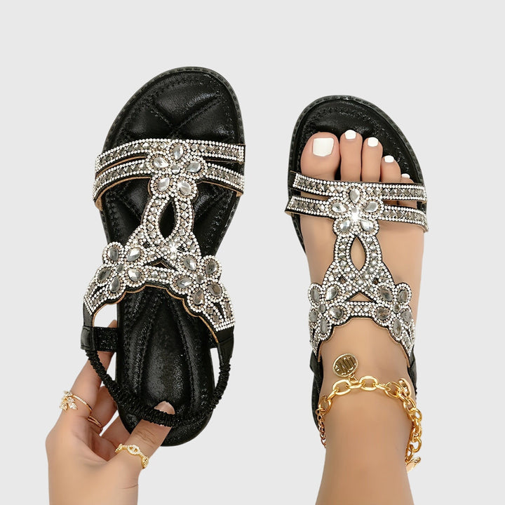 A woman wearing sky blue jewelled sandals with sparkling stones across the straps and a stretchy slingback.