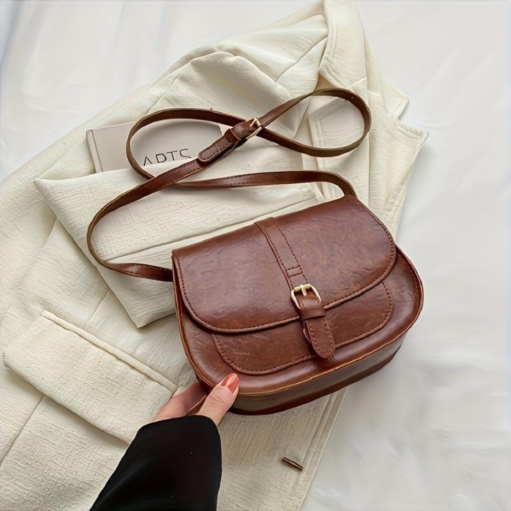 A woman carrying a crossbody satchel at her hip while out for a walk in town.