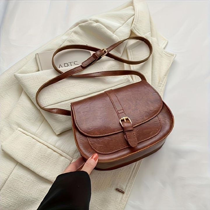 A woman carrying a crossbody satchel at her hip while out for a walk in town.