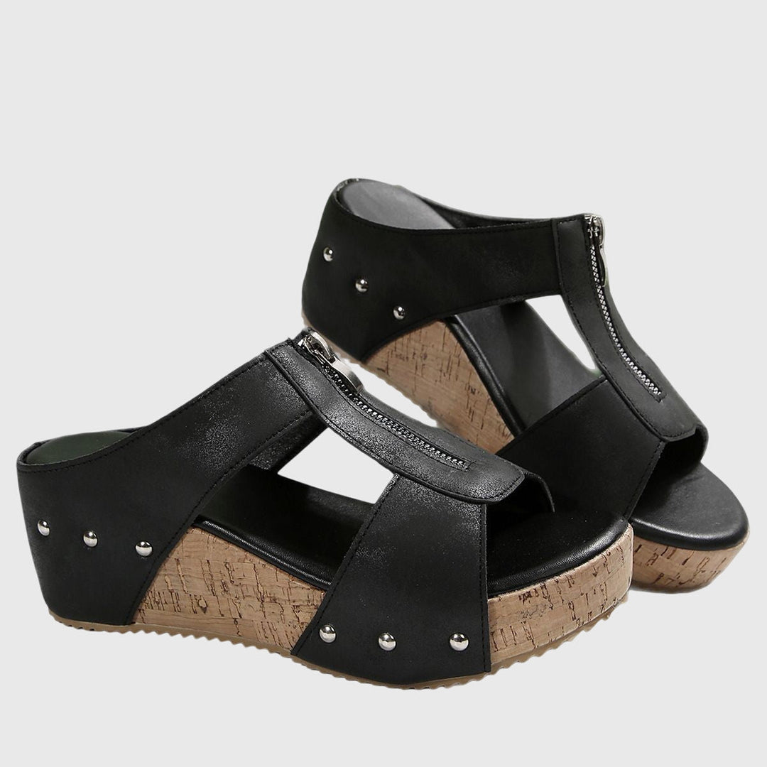 A woman wearing black zip-front wedge mules with a cushioned footbed and a broad platform sole.