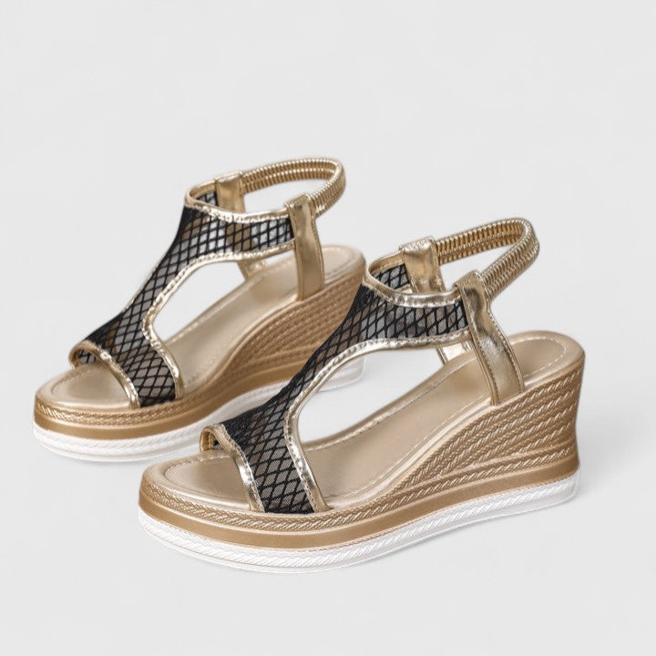 A woman wearing golden platform wedge sandals with a T-bar front, open-weave panels and a stretchy slingback.