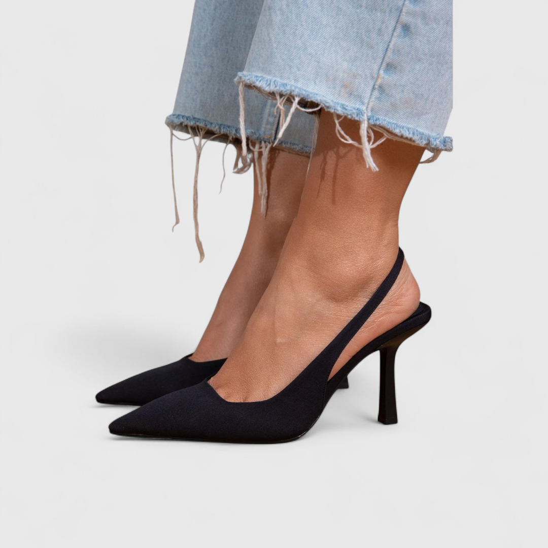 A woman wearing beige pointed slingback stilettos with a slim high heel.