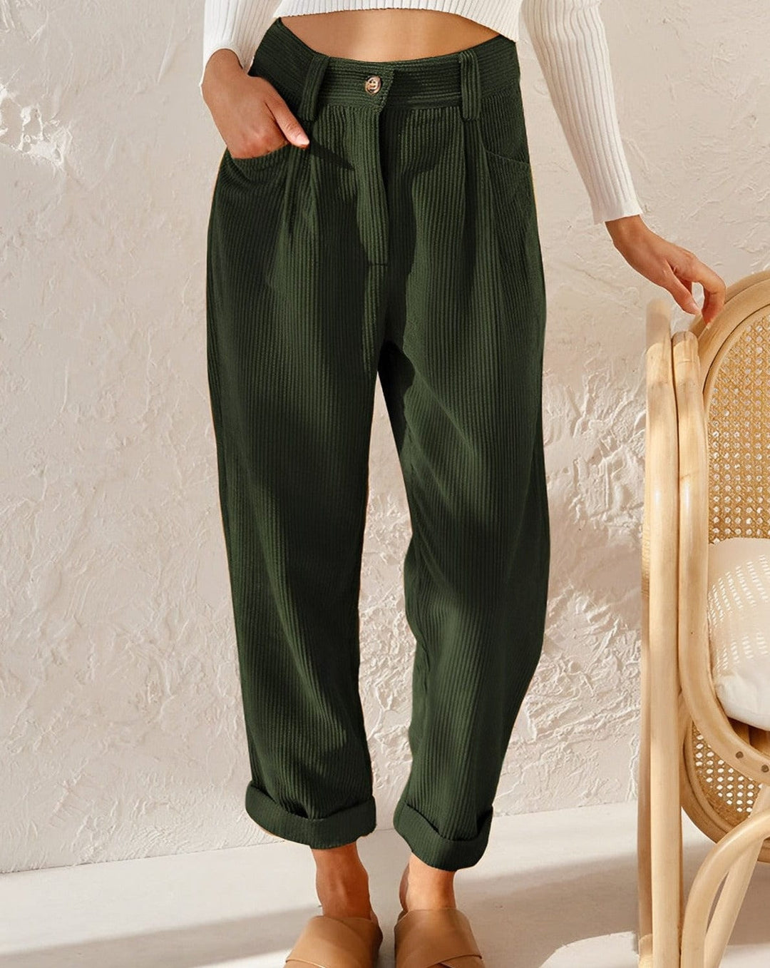 Woman wearing loose high-waisted pants with a tucked-in top, standing in soft light.
