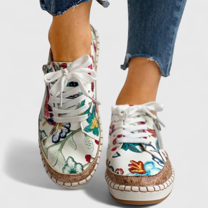 A woman wearing floral lace-up orthopaedic sneakers with a side zip and platform sole.