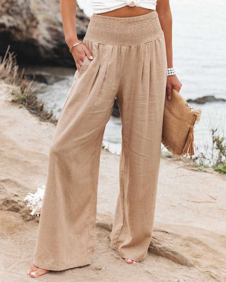 A woman walking by the sea in wide-leg beach pants with a relaxed, breezy summer look.