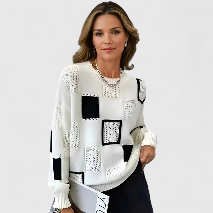 A woman wearing a white sweater with black geometric squares and openwork detailing, round neck.