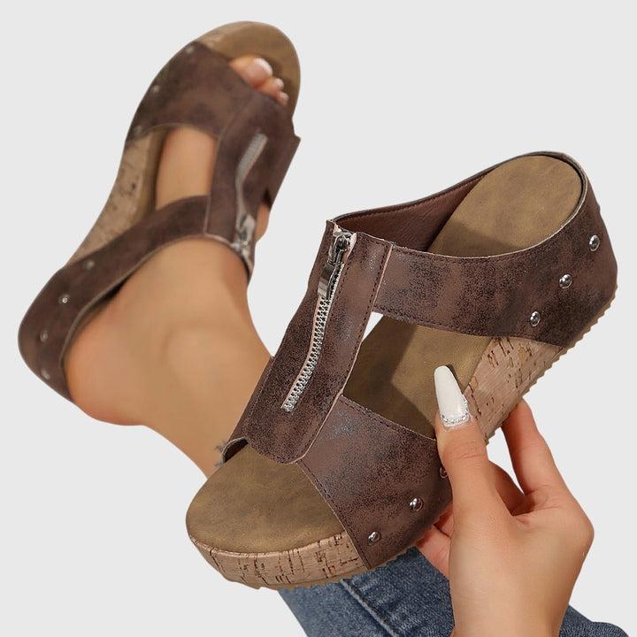 A woman wearing black zip-front wedge mules with a cushioned footbed and a broad platform sole.