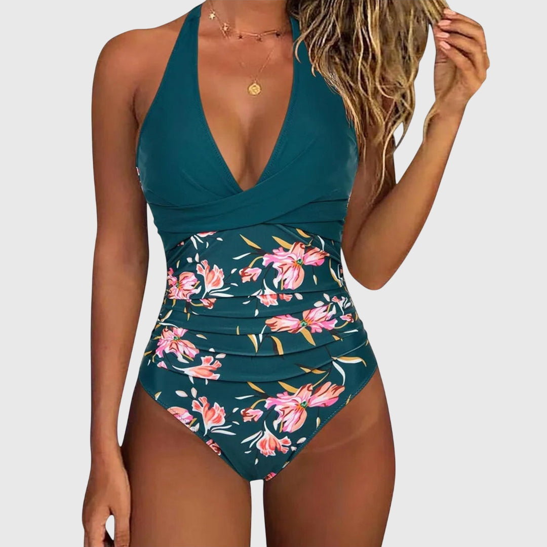 A woman by the sea in an elegant V-neck printed swimsuit, confident and relaxed in the sun.