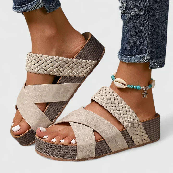 A woman strolling on a sunny street wearing beige woven comfort sandals with crossed straps.