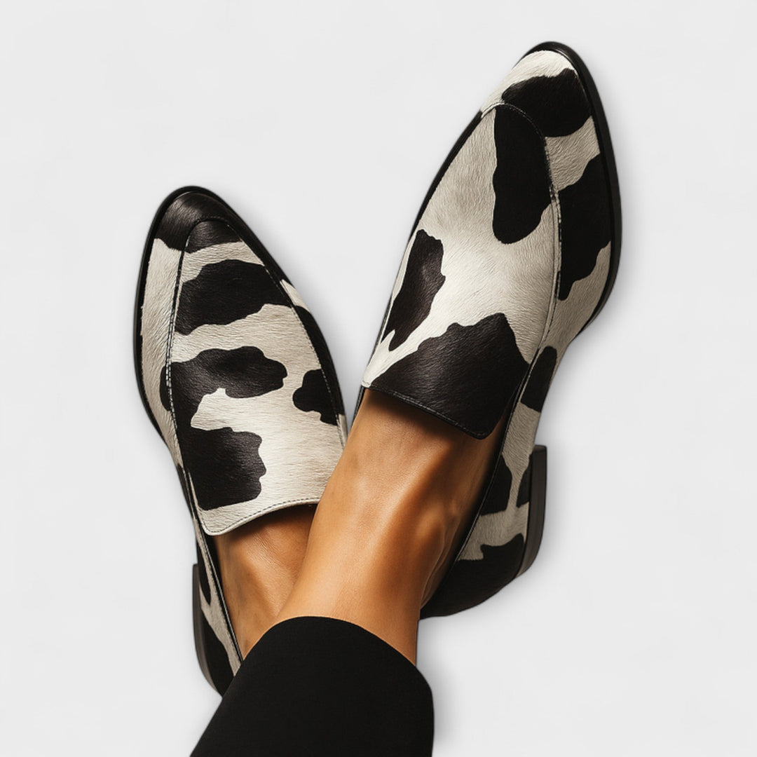 A woman wearing black-and-white cow-print loafers with a simple, modern outfit