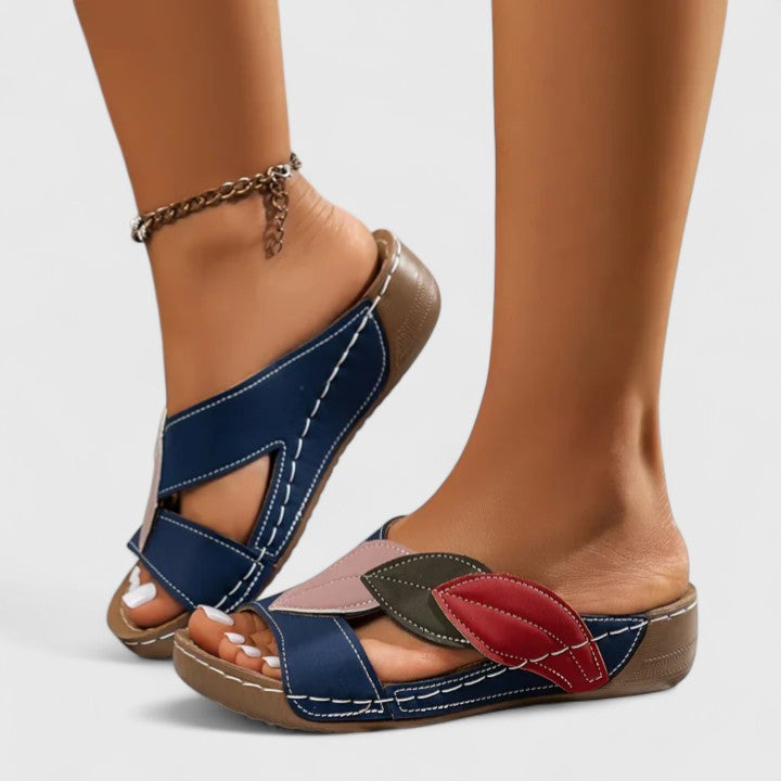 A woman wearing colourful leaf-print sandals with a cushioned insole and easy slip-on design.