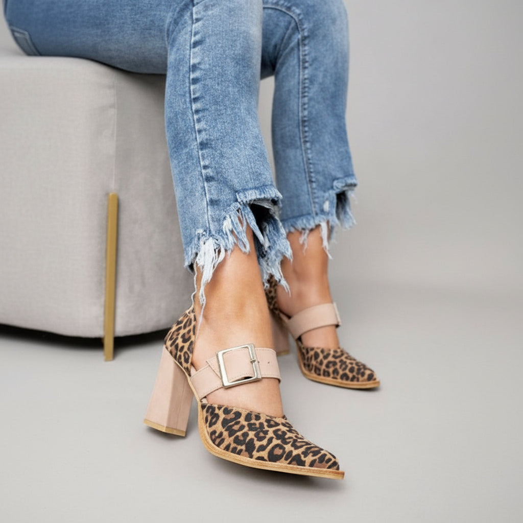 A woman wearing leopard print pointed-toe heels with a wide nude buckle strap and a neutral block heel.