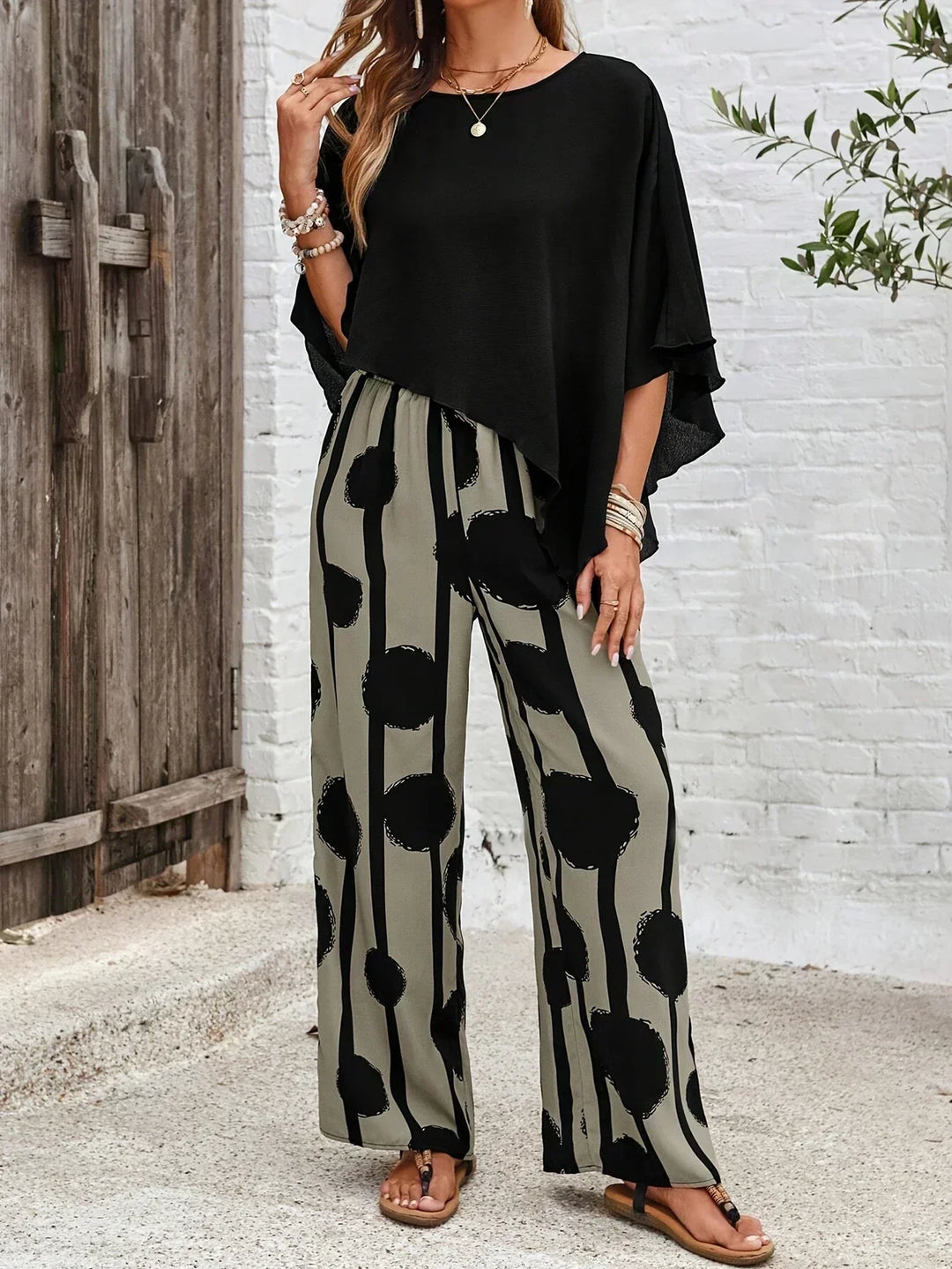 A woman wearing a draped asymmetric top with printed high-waisted wide-leg pants.