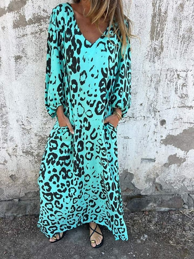 Woman in the Alison leopard print maxi dress with long sleeves and a V-neckline, walking along the shoreline.
