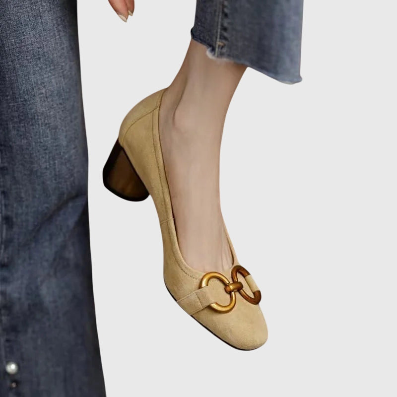 A woman wearing khaki block-heel court shoes with a gold buckle detail, standing with ease and confidence.