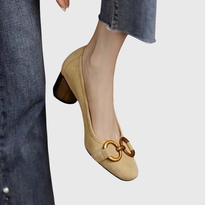A woman wearing khaki block-heel court shoes with a gold buckle detail, standing with ease and confidence.