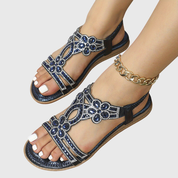A woman wearing sky blue jewelled sandals with sparkling stones across the straps and a stretchy slingback.